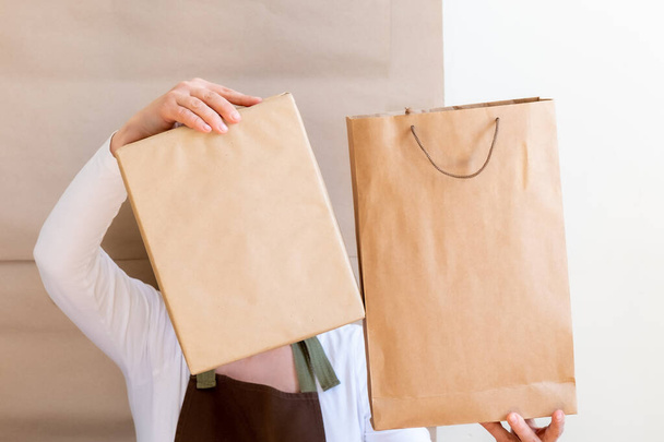 Les mains de Packer tenant un sac et une boîte en papier artisanal. Travailleur habillé en tablier brun Commande d'emballage pour le client
. - Photo, image