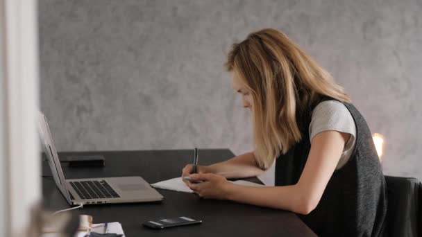 Young woman sitting at a Desk, online learning, laptop, and smartphone - Materiał filmowy, wideo