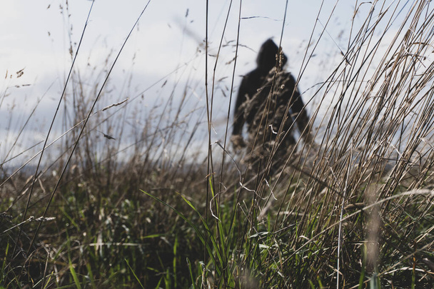 A sinister hooded figure standing in a field, out of focus. With a low camera angle. - Photo, Image