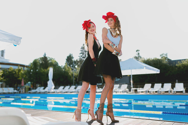 милые девушки в красных шляпах и купальнике рядом с бассейном под открытым небом с этническими аксессуарами и ювелирными изделиями, мягкий фокус, без бренда, пин-ап позируя
 - Фото, изображение