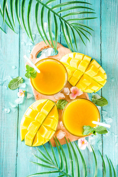 Friss nyári trópusi gyümölcsital. Mangó smoothie vagy mangó lé, friss mangóval és trópusi levelekkel kültéri fa háttéren. Másolja le a tér tetejét. - Fotó, kép