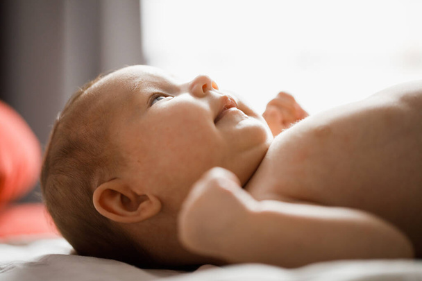 Closeup side profile backlit portrait of little baby lying in bed on her back - Fotó, kép