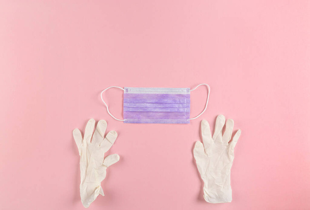 White latex gloves and blue face mask on pink background. Coronavirus prevention background. Copy space. - Photo, Image