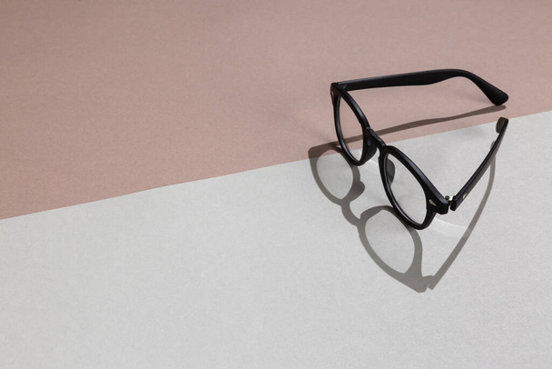 Black frame trendy eye glasses on gray and brown paper background. Hard light with shadow. Fashion accessory minimal concept. - 写真・画像