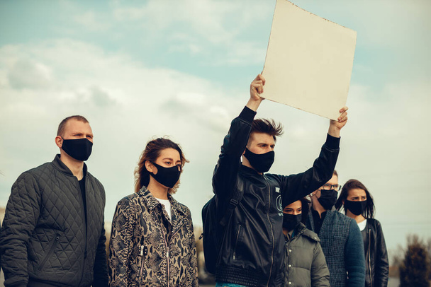 Ryhmä naamioituneita ihmisiä, jotka esittivät julisteita protestoidakseen väestön mielenosoitusta koronavirusta vastaan ja karanteenikokouksen järjestämistä vastaan koronaviruksesta ja ihmisten oikeuksista. Kopioi
 - Valokuva, kuva