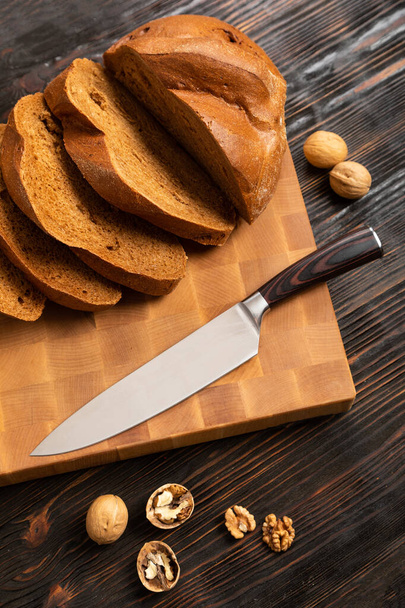 A loaf of bread sliced into slices with a knife on a wooden cutting board - Foto, Imagem