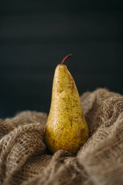 Still life with a pear standing on burlap on a dark wooden background. - Fotó, kép
