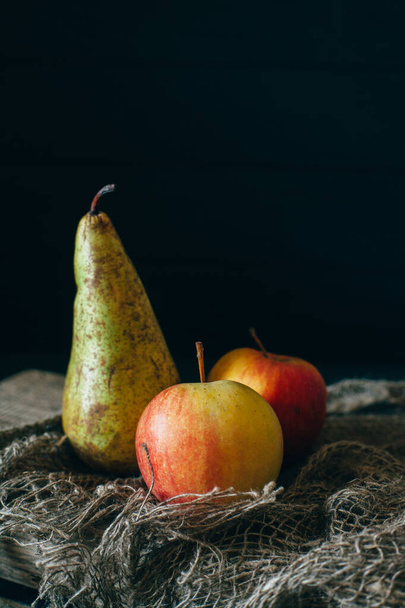 Still life with pears and apple on burlap on a dark wooden background. - Fotografie, Obrázek