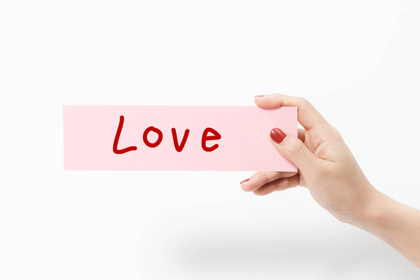 close up vrouwen houden roze papier met liefde tekst op witte achtergrond. - Foto, afbeelding