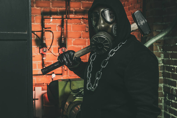Muž s plynovou maskou a kladivem ve strojovně. Koncept jaderného, biologického a chemického nebezpečí. - Fotografie, Obrázek