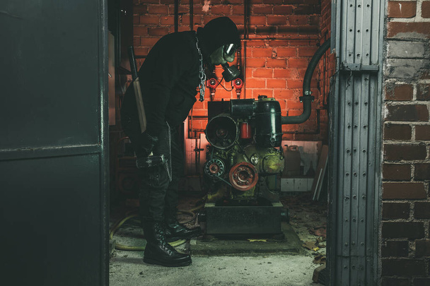 Homme avec masque à gaz et un marteau dans la salle des machines. Concept de danger nucléaire, biologique et chimique
. - Photo, image