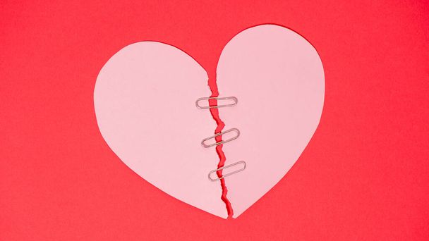 Красная бумага сердце разорвано пополам защищены зажимом безопасности на красном фоне
 - Фото, изображение