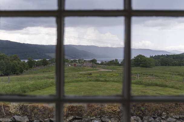 through a grid created by a wooden window we can see the outside landscape, a green meadow, the mountains and the cloudy sky - Photo, Image