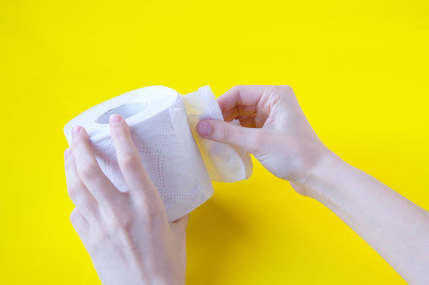 Hands tear a piece from a roll of white toilet paper on a yellow background - Photo, image