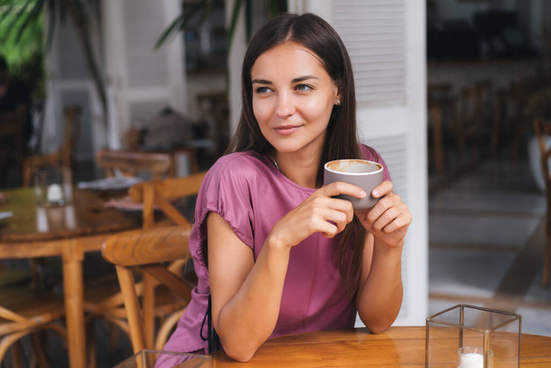 Portret pięknej kobiety pijącej gorący napój z filiżanki w kawiarni i uśmiechającej się - Zdjęcie, obraz