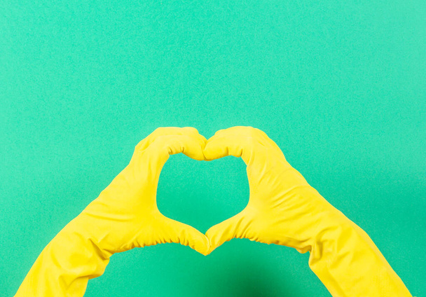 Hands in yellow rubber gloves making heart shape with fingers, on green background - Zdjęcie, obraz