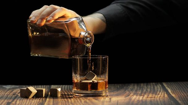 Whiskey, Cognac ins Glas gießen. Schwarzer Hintergrund. Viel Alkohol getrunken - Foto, Bild