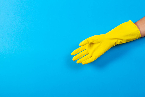 Bir kadın mavi arka planda sarı lastik eldiven takıyor. - Fotoğraf, Görsel
