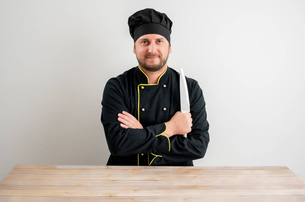 Joven chef de uniforme negro con el cuchillo en la mano posando sobre un fondo blanco y aislado
 - Foto, Imagen