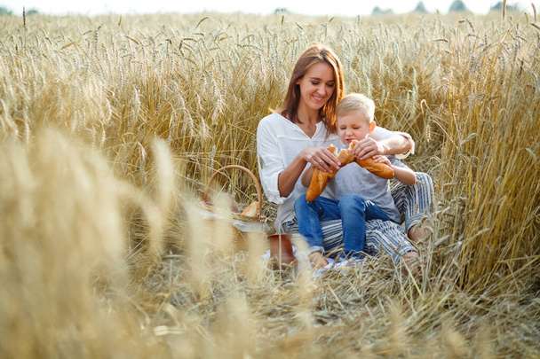 pique-nique en famille dans la nature lors d'un pique-nique en famille dans la nature un soir d'été. mère et fils mangent du pain, boivent le lait d'une cruche en céramique dans un champ de blé
 - Photo, image