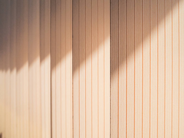 Textile lamellas of vertical blinds covering the window. Oblique rays of sunlight create an abstract pattern. Cozy, peaceful atmosphere. - Foto, Imagem