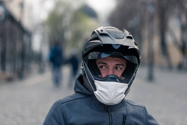 Portret mężczyzny w kasku. na kasku motocyklowym biała maska medyczna. zdjęcie na ulicy na tle domów. koronawirus, choroba, zakażenie, kwarantanna, kovid-19 - Zdjęcie, obraz