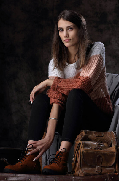 Portrait of a beautiful girl in winter boots and a sweater with an old leather bag - Foto, Imagen