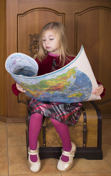 A menina senta-se em um peito e considera o mapa mundial
 - Foto, Imagem