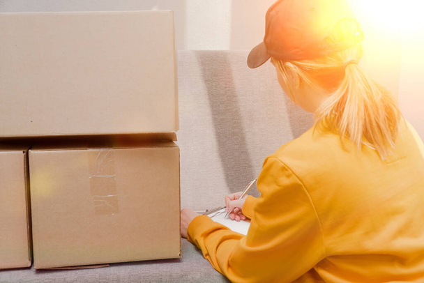 a girl on a sunny day in a black cap signs documents for sending boxes on a sunny day. online order delivery - 写真・画像