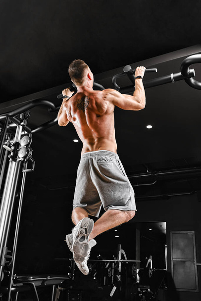 Bodybuilder does pull-ups. Muscular man in the gym. Preparation for competitions, functional training. The athlete is gaining his form. - Foto, afbeelding