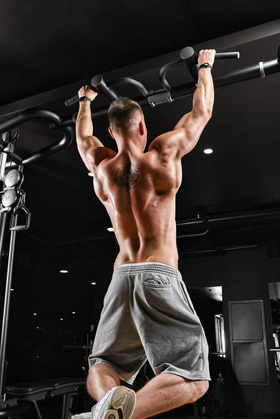 Bodybuilder does pull-ups. Muscular man in the gym. Preparation for competitions, functional training. The athlete is gaining his form. - Foto, Bild