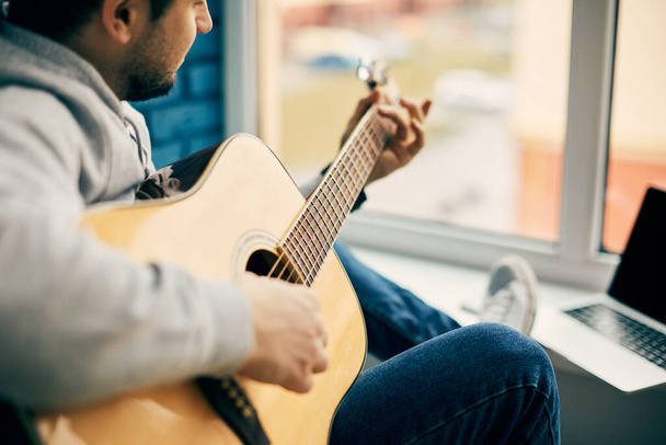 крупным планом гитары и мужчины рука играет на нем на балконе и синем фоне стены
 - Фото, изображение