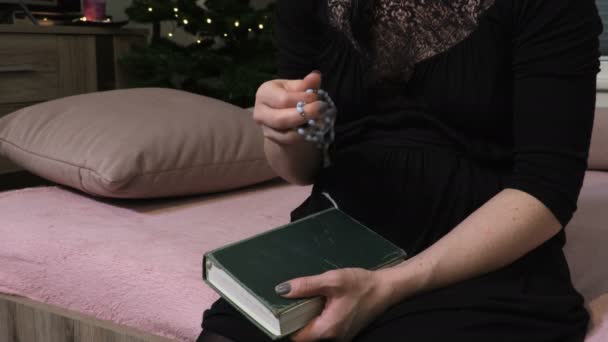 Женщина сидит на кровати и держит четки и Библию - Кадры, видео