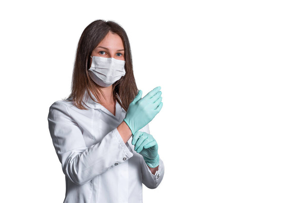 Young female nurse on camera wearing a surgical or medical mask. Doctor wearing a white bathrobe and gloves isolated on white background. covid 19, coronavirus, quarantine - Photo, image