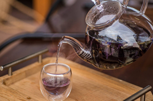 Fioletowy kwiatowy herbata ziołowa jest wlewana z browara do filiżanki. - Zdjęcie, obraz
