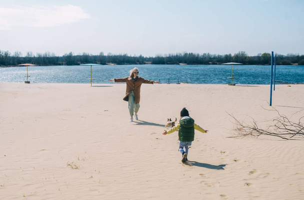 Мать, дочка и собачка развлекаются на песчаном пляже у реки.
. - Фото, изображение