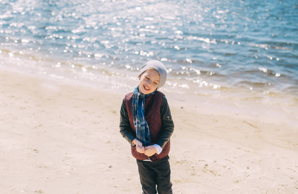 Szczęśliwy chłopczyk stojący na piaskowej plaży. Szczęście na wiosennych wakacjach nad rzeką, emocje. Widok z góry - Zdjęcie, obraz