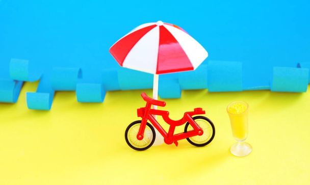 Red toy bicycle and beach umbrells with summer cocktail against sea. Summer rest. Vacations near sea - Foto, immagini