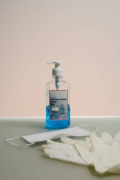 Pullo kirkasta nestettä antibakteerinen käsi geeli. Antibakteerinen käsi puhdistusaine, lääketieteelliset käsineet ja naamio pöydällä
 - Valokuva, kuva