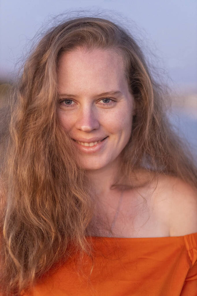 Portret van een mooie vrouw, meisje bij zonsondergang. Het meisje draagt een oranje blouse. Het haar komt uit de wind.. - Foto, afbeelding