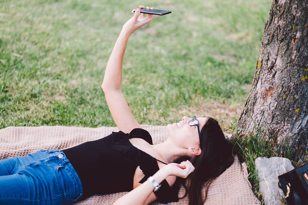 Nuori nainen rentouttava kesäpuistossa älypuhelimella - Valokuva, kuva