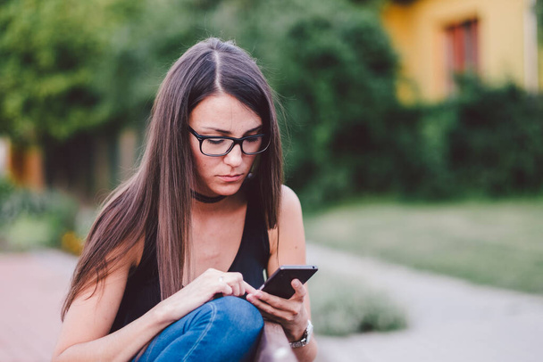 fiatal nő használja okostelefonját, miközben ül a padon - Fotó, kép