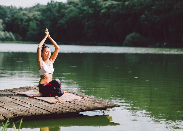 Молодая женщина практикующая йогу в позе лотоса на озере - Фото, изображение