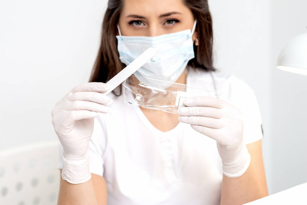 Frau mit medizinischem Werkzeug trägt Maske im Salon. - Foto, Bild