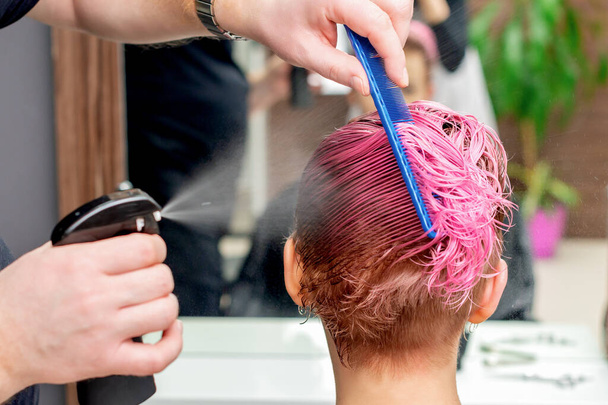 Ręce fryzjera kropią wodą na różowe włosy kobiety.. - Zdjęcie, obraz