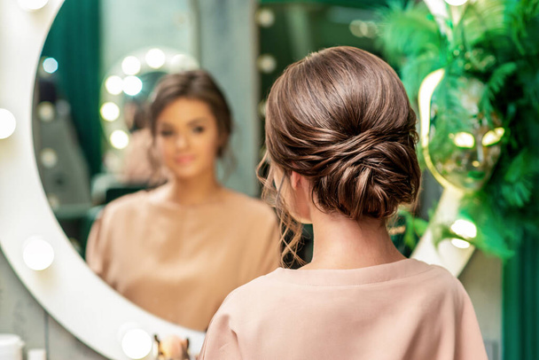 Beautiful young woman with hairstyle looking in the mirror at beauty salon. - Φωτογραφία, εικόνα