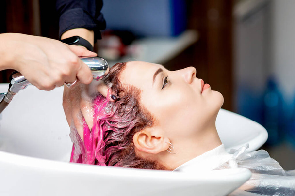 Friseurhände waschen rosa gefärbte Haare einer Frau im Waschbecken, Nahaufnahme. - Foto, Bild