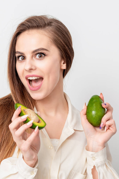 Portrait of pleasantly surprised woman with a two avocado on white background. - Foto, immagini