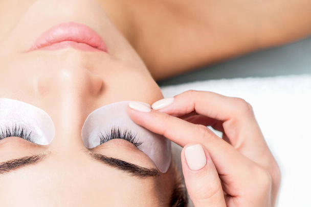 Kosmetologi käsi liimaa ilmastointiteippiä silmien alla nuori nainen kasvot ennen silmäripsien laajennus menettely, ylhäältä
. - Valokuva, kuva