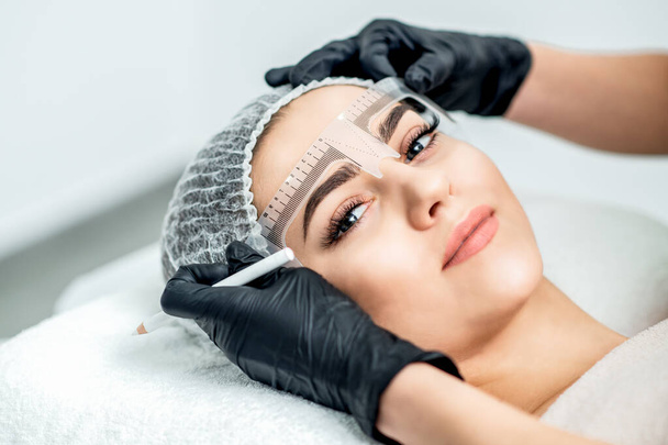 Kalıcı makyaj sırasında genç bir kadının kaşlarında cetvel olan bir marka.. - Fotoğraf, Görsel